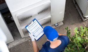 An HVAC technician holding a clipboard and working on a commercial HVAC system.