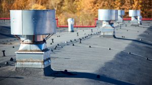 Air roof exhaust ventilation fan system of industrial large commercial building with hooded chimneys flues and ducts in row on roof top selective focus with lightning protection system.