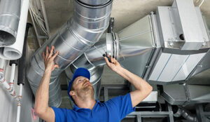 Man in blue shirt and hat examining hvac vents attached to ceiling